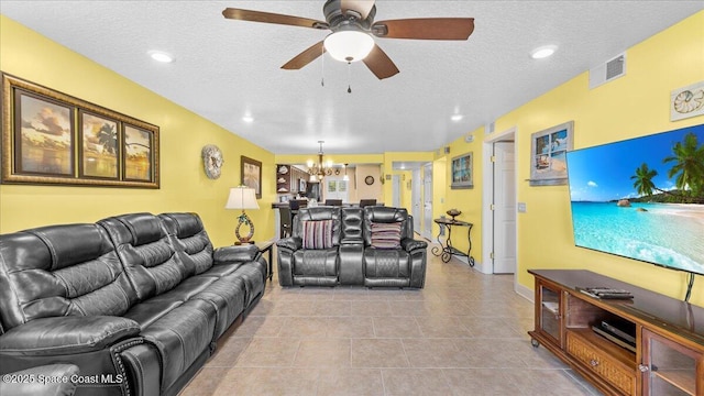 tiled living area featuring a textured ceiling, ceiling fan with notable chandelier, and visible vents