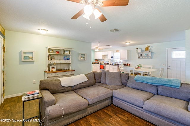 living room with dark wood-style floors, visible vents, ceiling fan, and baseboards