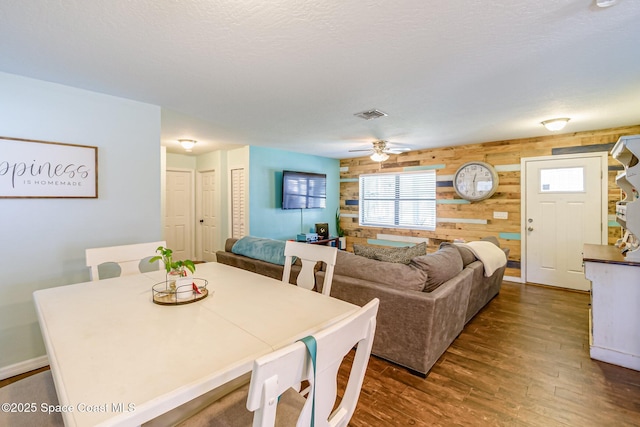 dining room featuring visible vents, dark wood-type flooring, ceiling fan, wood walls, and a textured ceiling