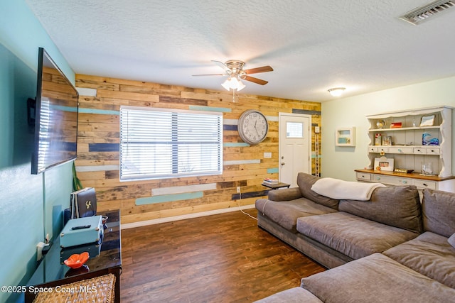 living area with visible vents, wood walls, a textured ceiling, and wood finished floors