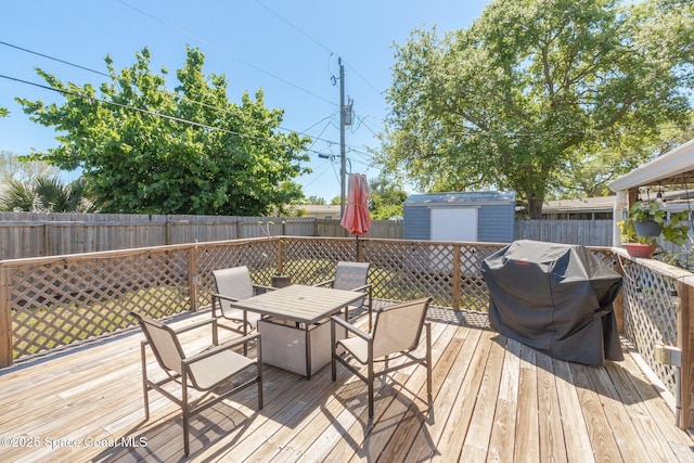 deck featuring outdoor dining space, a fenced backyard, a shed, grilling area, and an outdoor structure