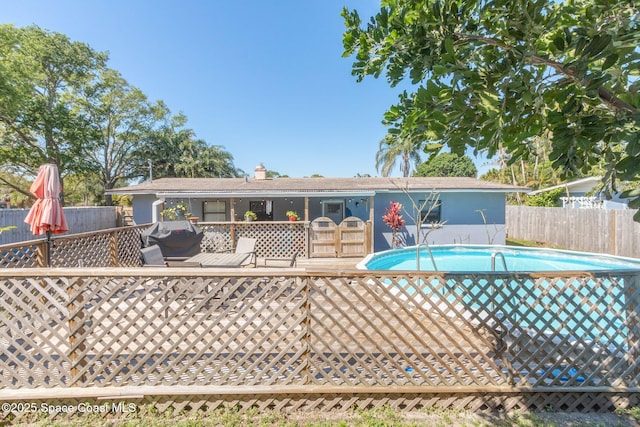 rear view of property with a fenced in pool, a deck, and fence