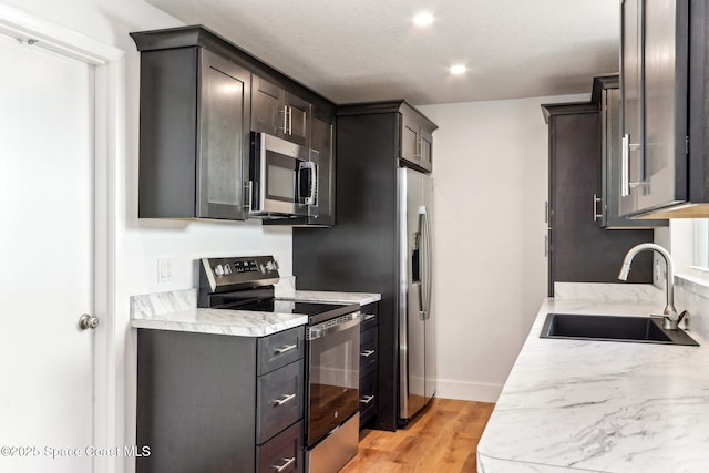 kitchen featuring baseboards, light wood-style flooring, a sink, stainless steel appliances, and light countertops