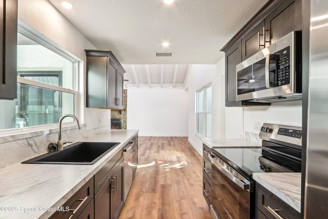 kitchen featuring visible vents, a sink, stainless steel appliances, dark brown cabinetry, and light wood-type flooring