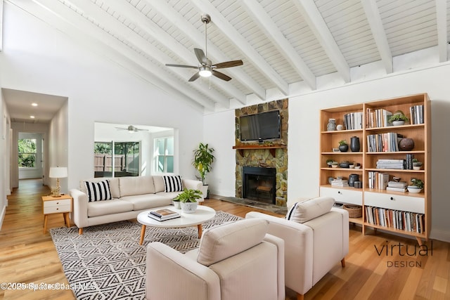 living room with beamed ceiling, a stone fireplace, ceiling fan, and light wood finished floors