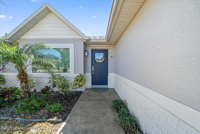 view of exterior entry with brick siding and stucco siding