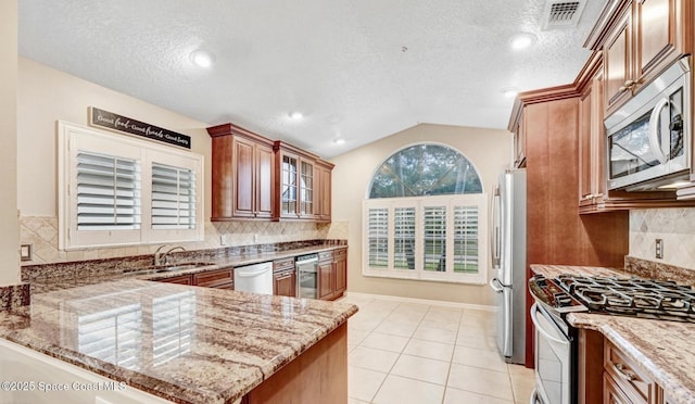 kitchen featuring stainless steel appliances, visible vents, vaulted ceiling, light stone countertops, and a peninsula