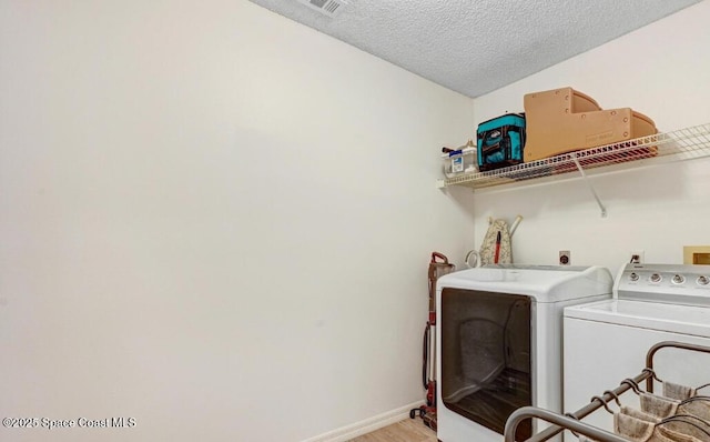 washroom with light wood finished floors, a textured ceiling, separate washer and dryer, laundry area, and baseboards