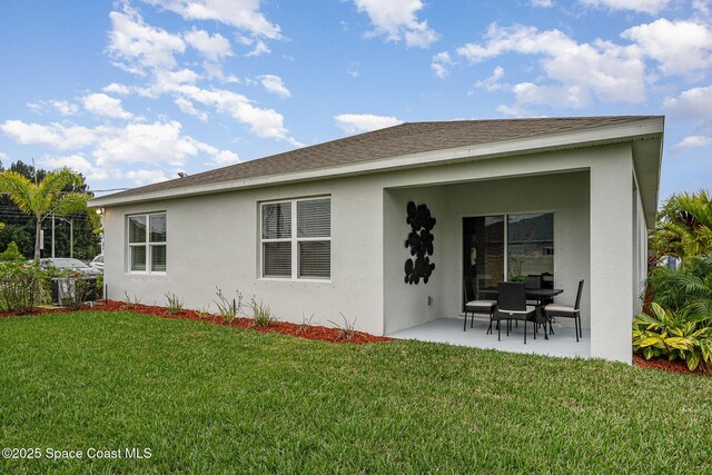 back of property with stucco siding, roof with shingles, a lawn, and a patio