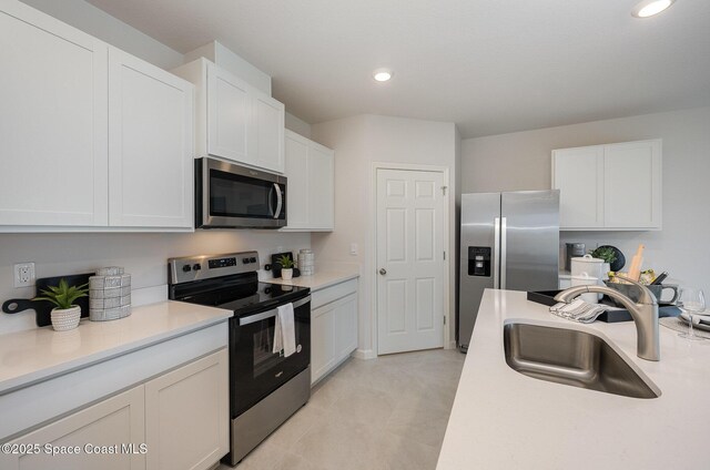 kitchen featuring white cabinets, stainless steel appliances, a sink, and light countertops