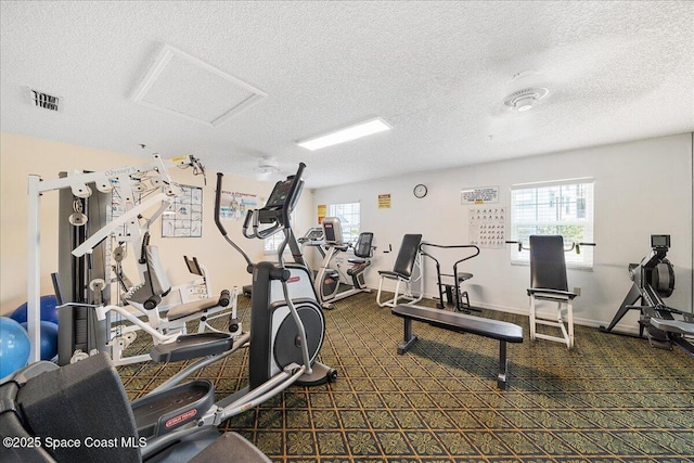 exercise room featuring attic access, a textured ceiling, visible vents, and a wealth of natural light