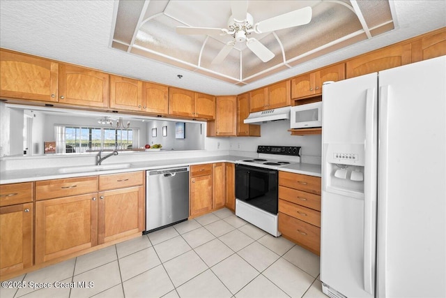 kitchen with a raised ceiling, light countertops, a sink, white appliances, and under cabinet range hood