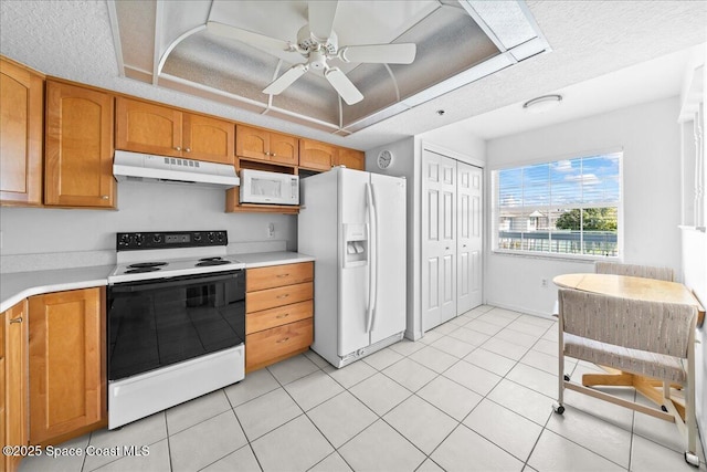 kitchen featuring white appliances, brown cabinetry, a tray ceiling, light countertops, and under cabinet range hood