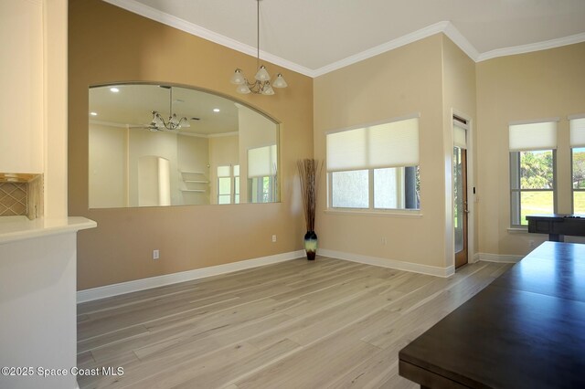 unfurnished room with a chandelier, wood finished floors, baseboards, ornamental molding, and a wealth of natural light