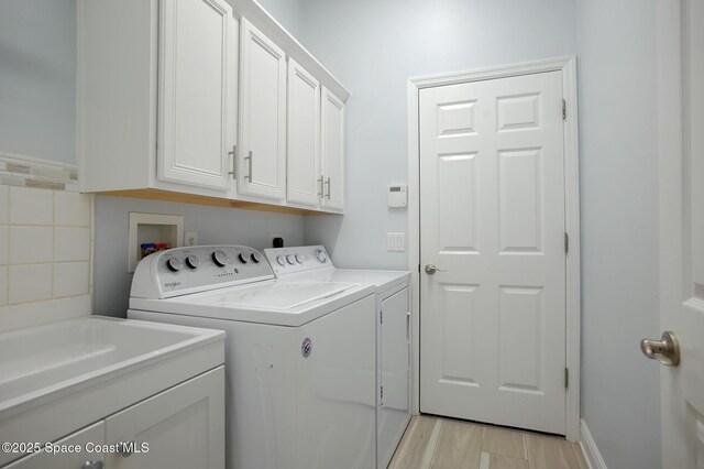 washroom featuring cabinet space, independent washer and dryer, light wood-style flooring, and a sink