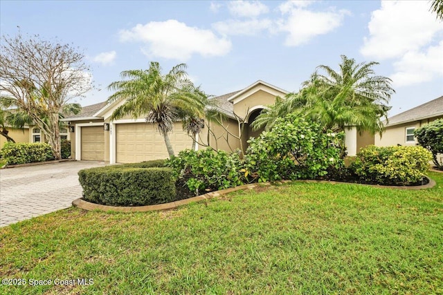 view of property hidden behind natural elements with decorative driveway, an attached garage, a front lawn, and stucco siding