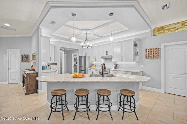 kitchen with visible vents, freestanding refrigerator, a sink, under cabinet range hood, and a kitchen bar