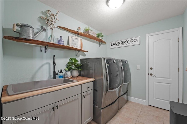 washroom featuring washer and clothes dryer, light tile patterned floors, cabinet space, a sink, and a textured ceiling