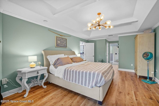 bedroom with wood finished floors, baseboards, a tray ceiling, an inviting chandelier, and crown molding