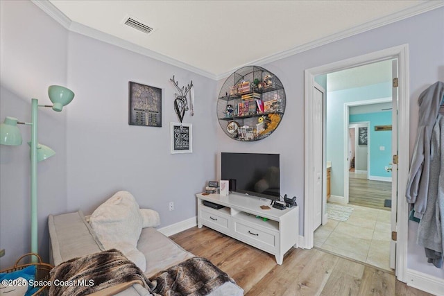 sitting room with ornamental molding, light wood-type flooring, visible vents, and baseboards