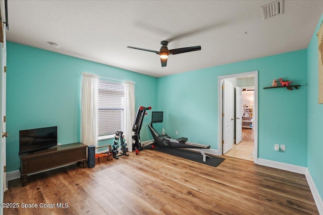 exercise room with visible vents, baseboards, ceiling fan, wood finished floors, and a textured ceiling