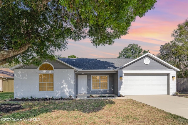 ranch-style home featuring a garage, brick siding, driveway, and a lawn