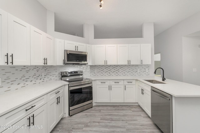 kitchen featuring a peninsula, a sink, stainless steel appliances, light countertops, and backsplash