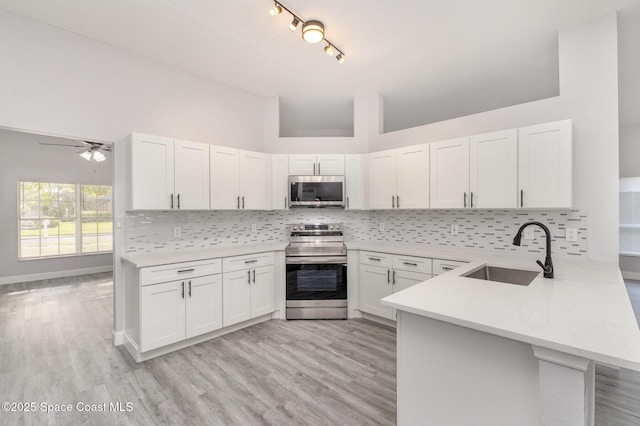 kitchen with backsplash, light countertops, a peninsula, stainless steel appliances, and a sink