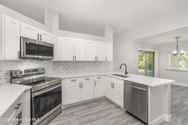 kitchen with light countertops, decorative backsplash, appliances with stainless steel finishes, a peninsula, and a sink