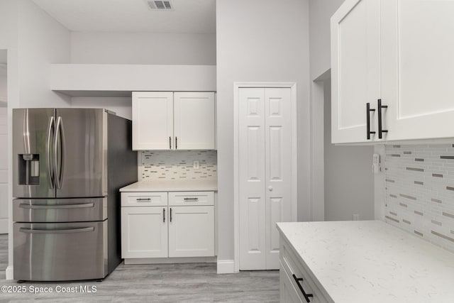 kitchen with decorative backsplash, light stone countertops, white cabinets, and stainless steel refrigerator with ice dispenser