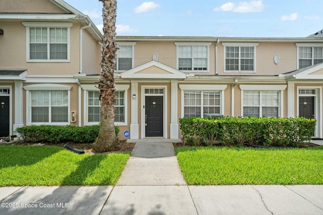 townhome / multi-family property featuring a front lawn and stucco siding