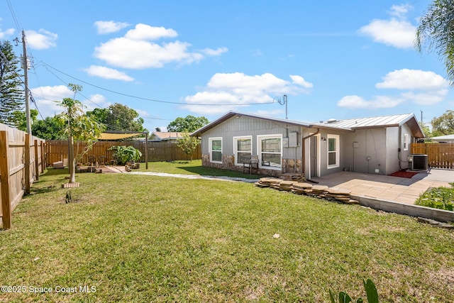 rear view of property featuring metal roof, a fenced backyard, a patio, and a lawn