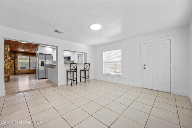 interior space with light tile patterned floors, visible vents, appliances with stainless steel finishes, a breakfast bar area, and a textured ceiling