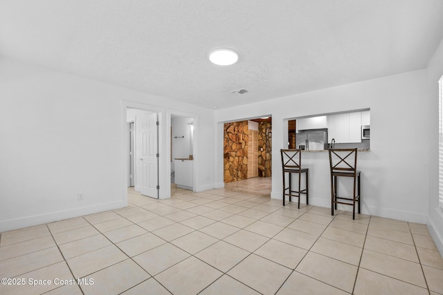 spare room featuring light tile patterned floors, baseboards, visible vents, and a textured ceiling