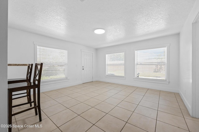 unfurnished dining area featuring a healthy amount of sunlight, light tile patterned floors, baseboards, and a textured ceiling