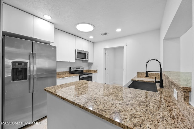 kitchen with stainless steel appliances, a peninsula, a sink, white cabinetry, and light stone countertops