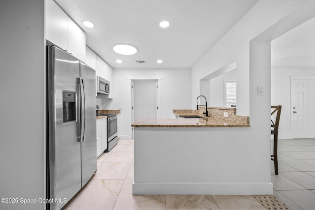 kitchen with light stone countertops, stainless steel appliances, white cabinetry, a sink, and recessed lighting