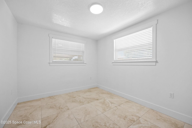 empty room featuring plenty of natural light, a textured ceiling, and baseboards