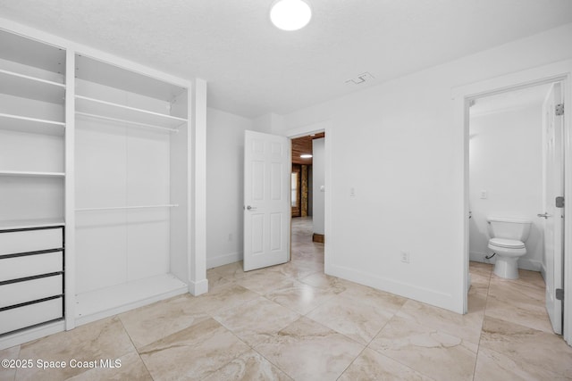 unfurnished bedroom with a textured ceiling, visible vents, baseboards, a closet, and ensuite bath