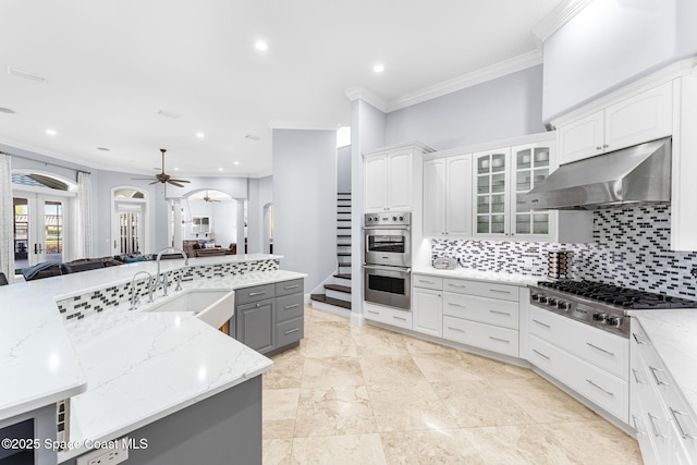 kitchen featuring gray cabinetry, under cabinet range hood, a sink, open floor plan, and stainless steel appliances