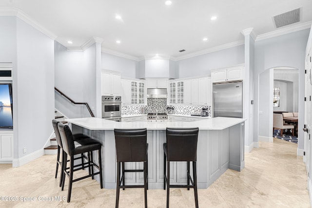 kitchen featuring visible vents, under cabinet range hood, decorative backsplash, appliances with stainless steel finishes, and arched walkways