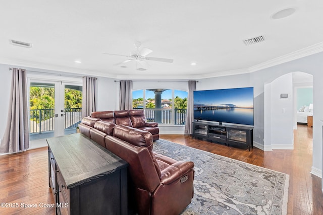 living room featuring arched walkways, visible vents, ornamental molding, and wood-type flooring