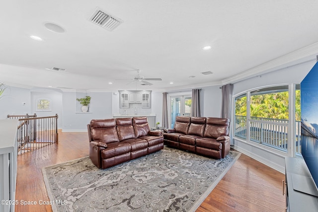 living area with baseboards, wood finished floors, visible vents, and ornamental molding