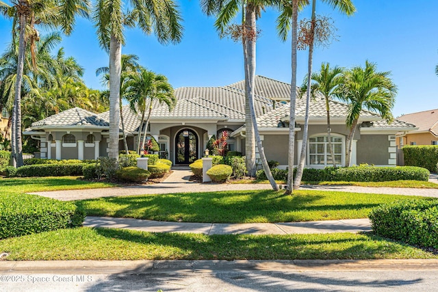 mediterranean / spanish-style house with a front yard, a tile roof, and stucco siding