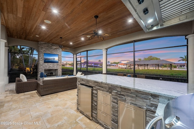 view of patio / terrace with a lanai, an outdoor living space with a fireplace, exterior kitchen, and a ceiling fan