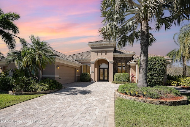 mediterranean / spanish home featuring a garage, stone siding, french doors, decorative driveway, and stucco siding