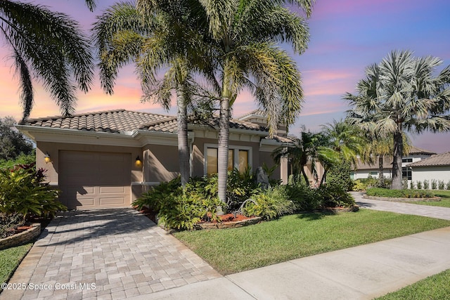 mediterranean / spanish home featuring a garage, a tiled roof, decorative driveway, stucco siding, and a front yard