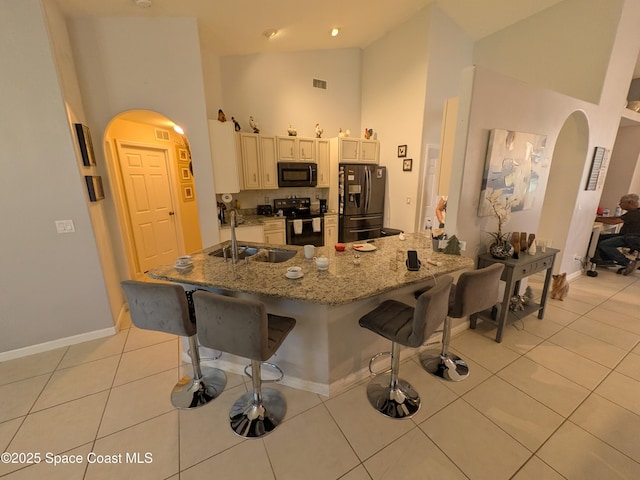 kitchen with light tile patterned floors, arched walkways, black appliances, a kitchen bar, and a sink