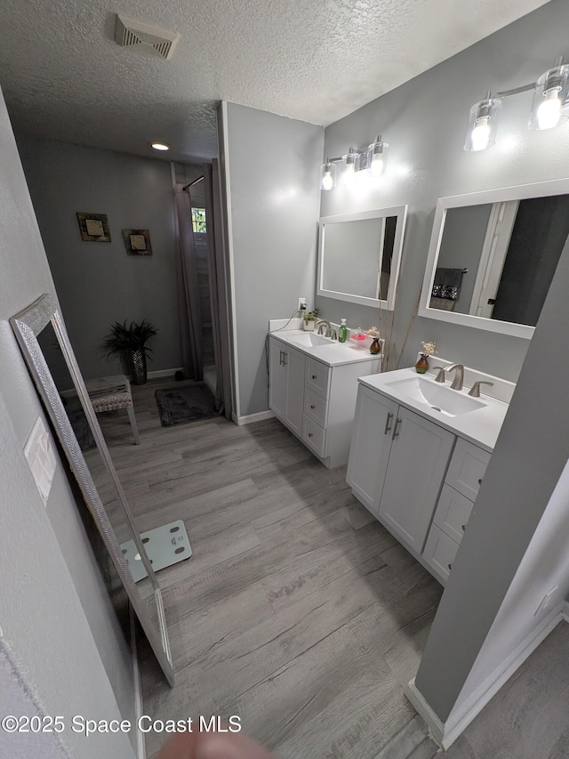 full bath featuring visible vents, wood finished floors, a sink, a textured ceiling, and two vanities