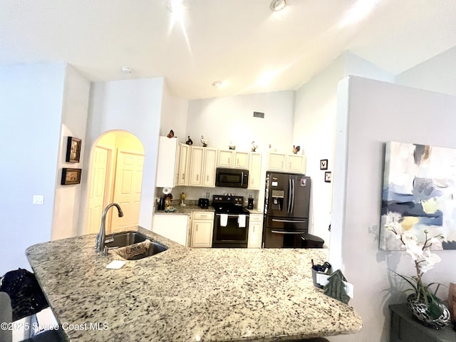 kitchen with a sink, visible vents, vaulted ceiling, cream cabinetry, and black appliances